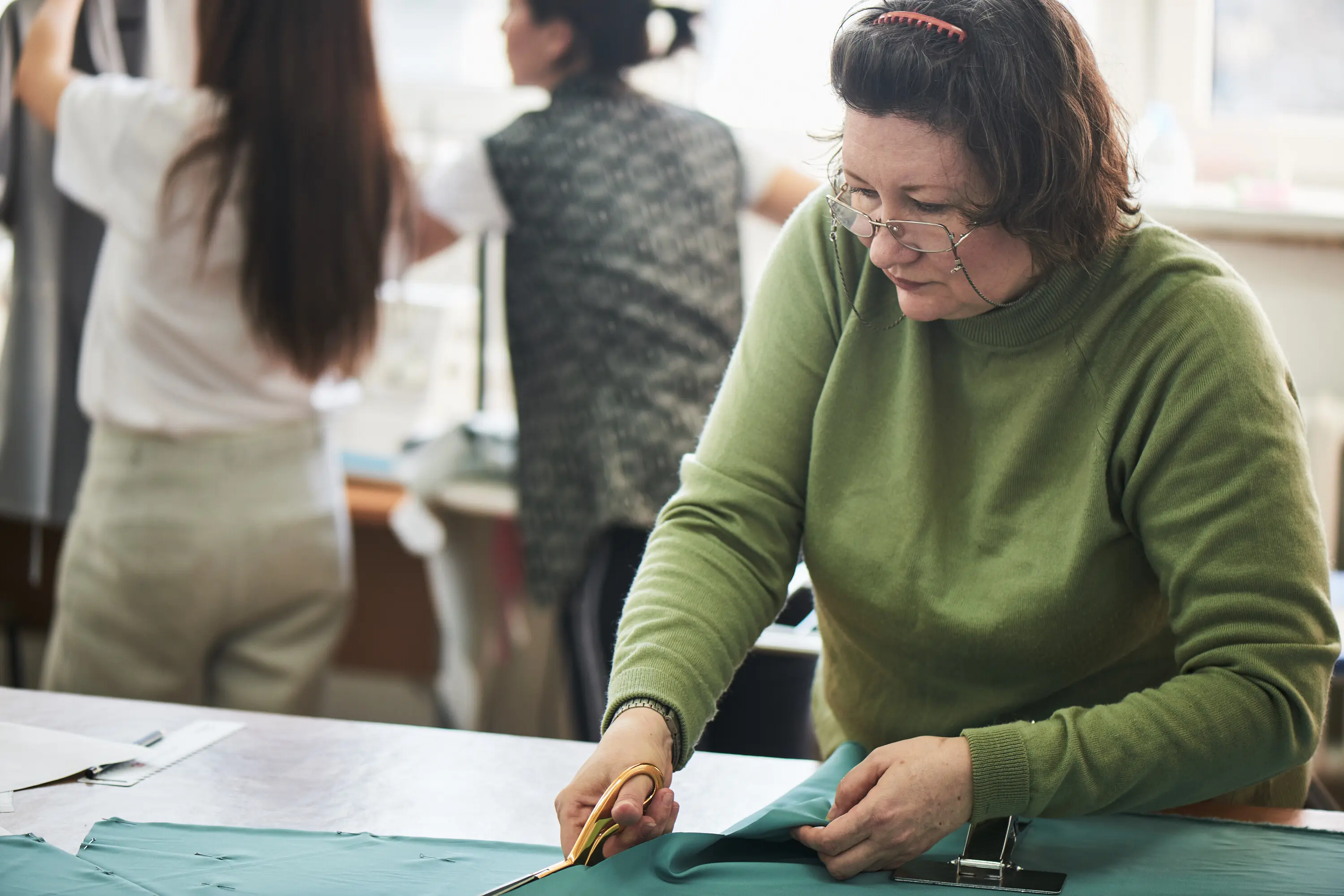 Die Näherin schneidet den Stoff mit der Stoffschere auf dem Tisch.